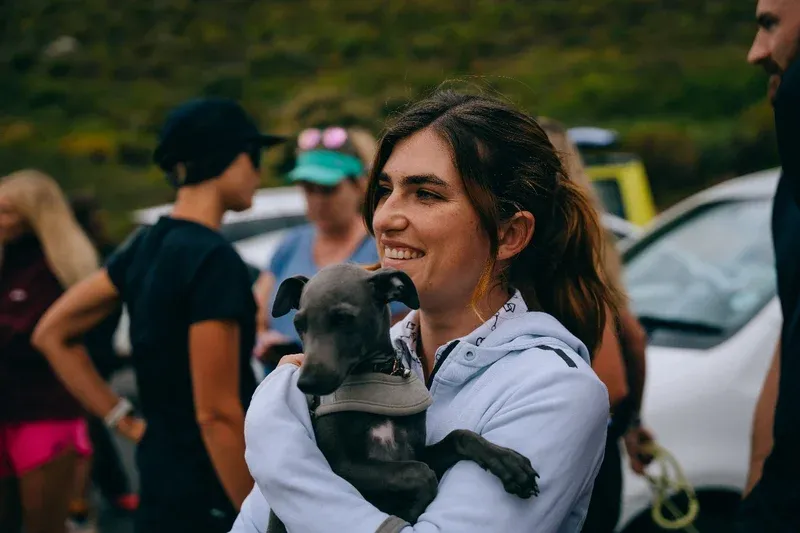 Leopards member smiling and holding a grey whippet puppy after a run