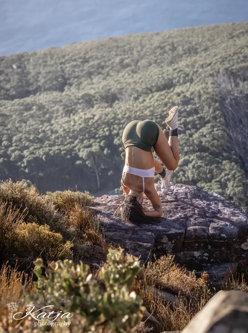 Leopards member doing a headstand on a mountain ledge overlooking the ocean